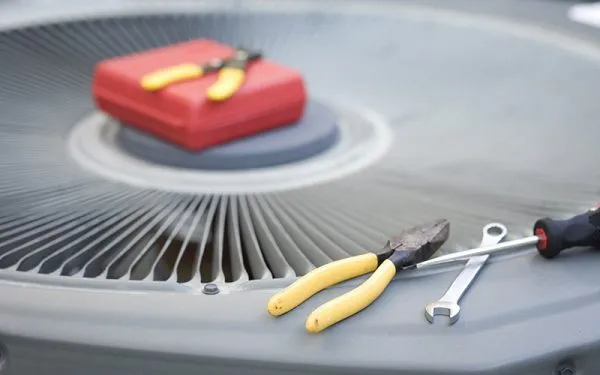 Air conditioner condenser top with yellow-handled pliers, wrench, screwdriver and red tool case