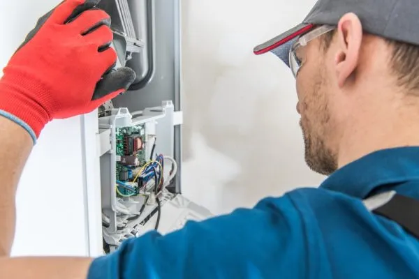 A technician repairs an appliance's exposed circuit board, wearing red gloves and safety glasses.