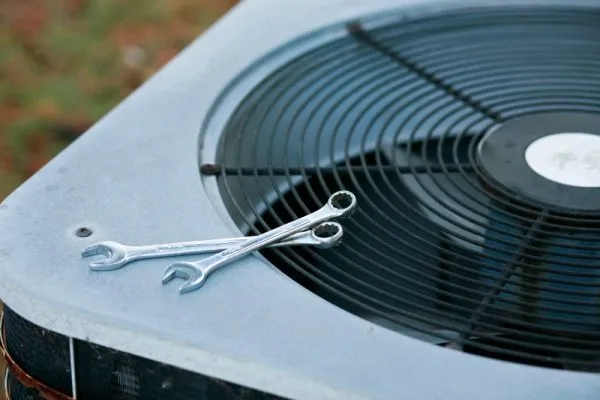 Two wrenches resting on the fan grill of an outdoor air conditioner condenser during HVAC maintenance